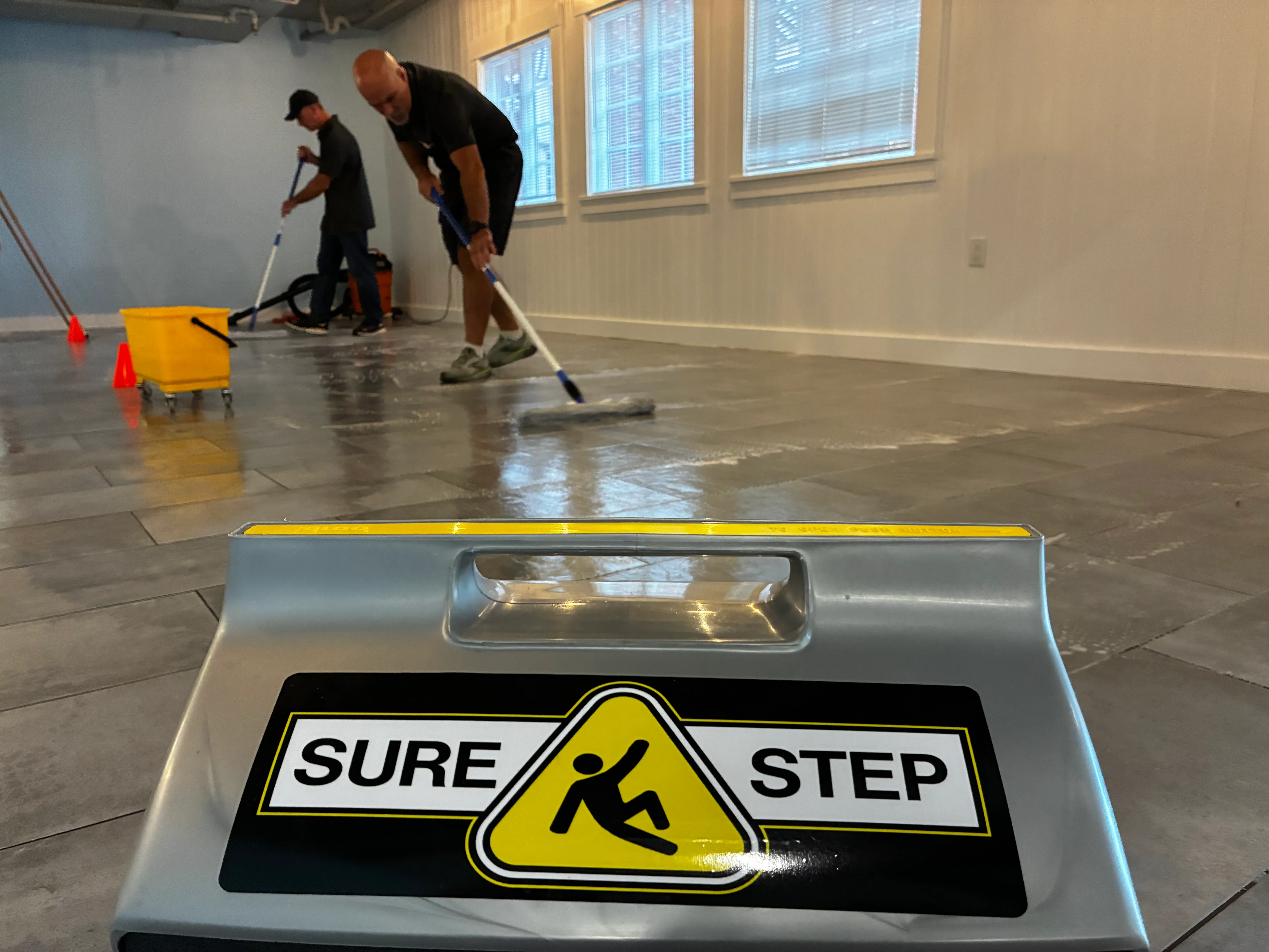 Workers applying Sure Step anti-slip epoxy coating to concrete floor with wet cleaning equipment
