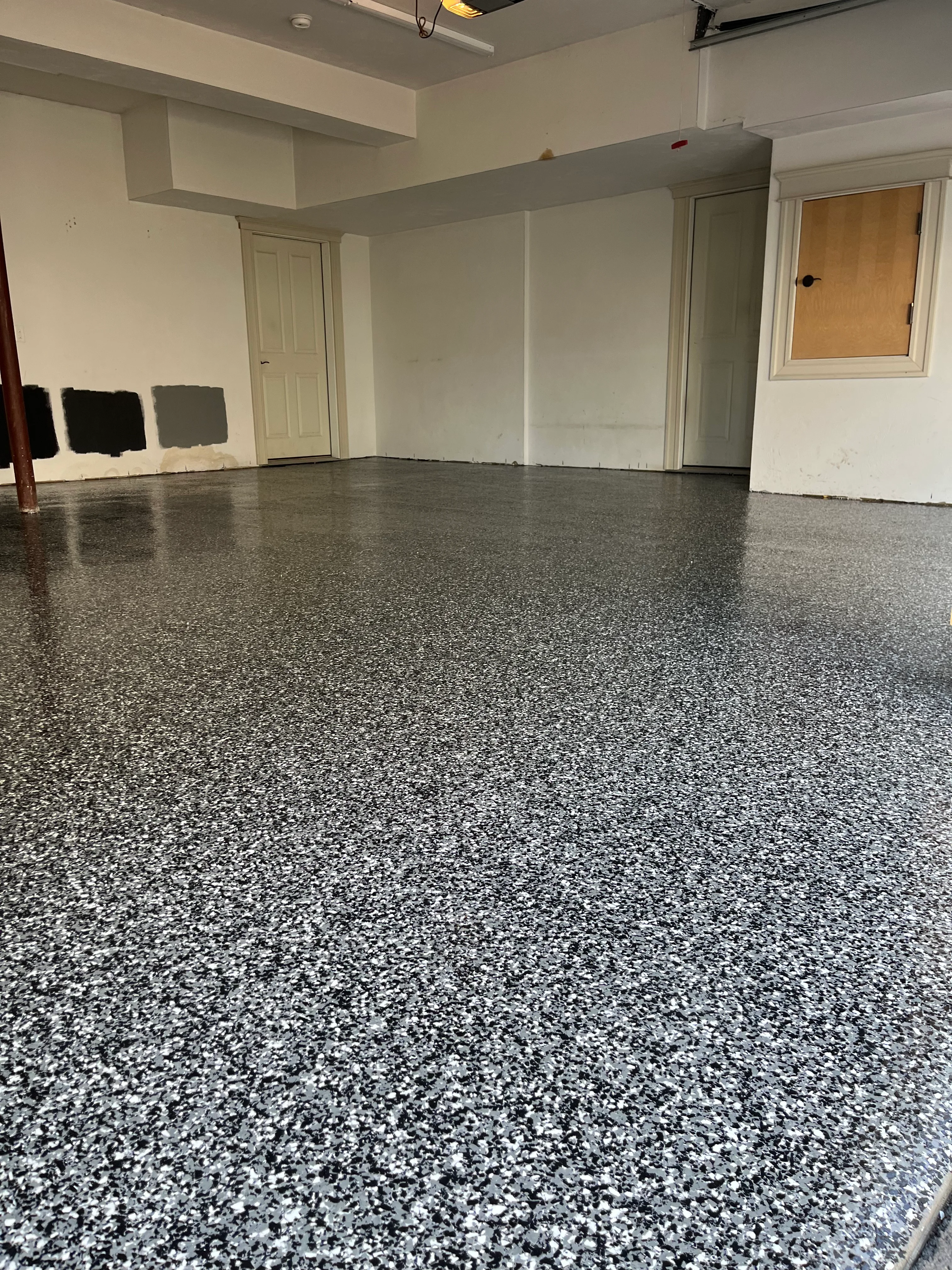 Finished gray speckled epoxy floor in basement garage with white walls and exposed beam