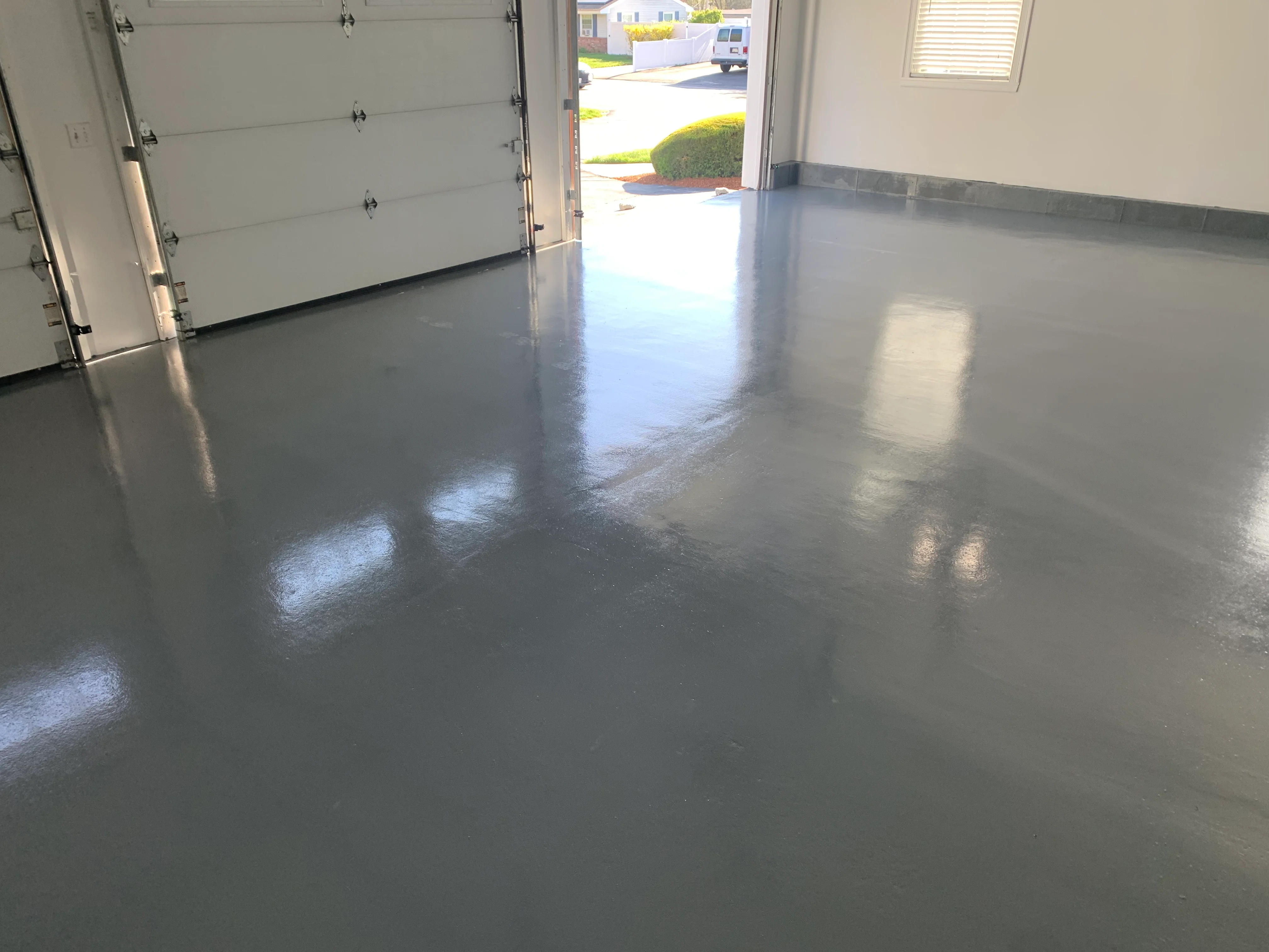 Polished gray epoxy garage floor with reflective finish and white garage door