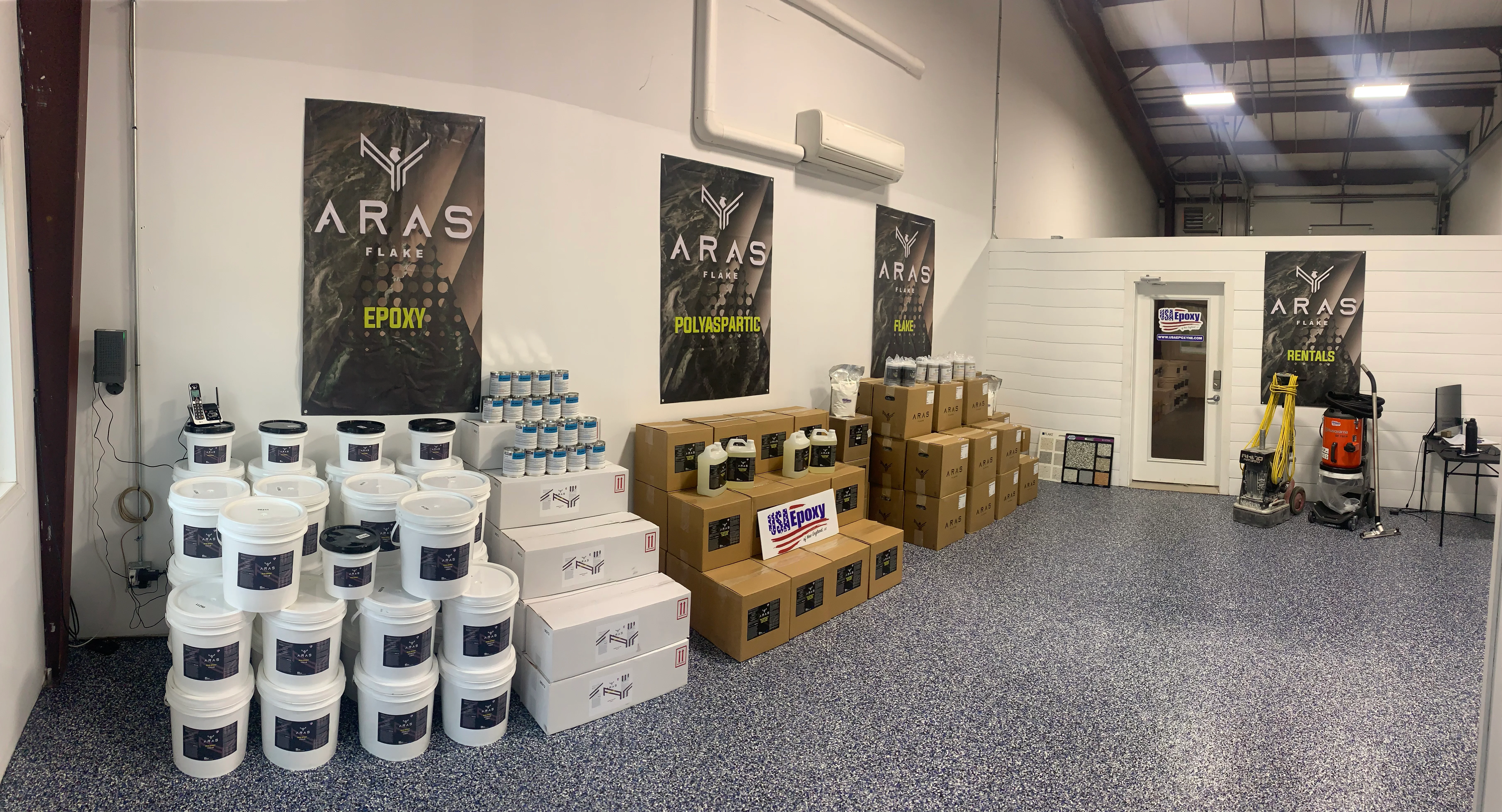 Showroom with epoxy buckets, polyaspartic products, cardboard inventory boxes, and ARAS Flake branded signage