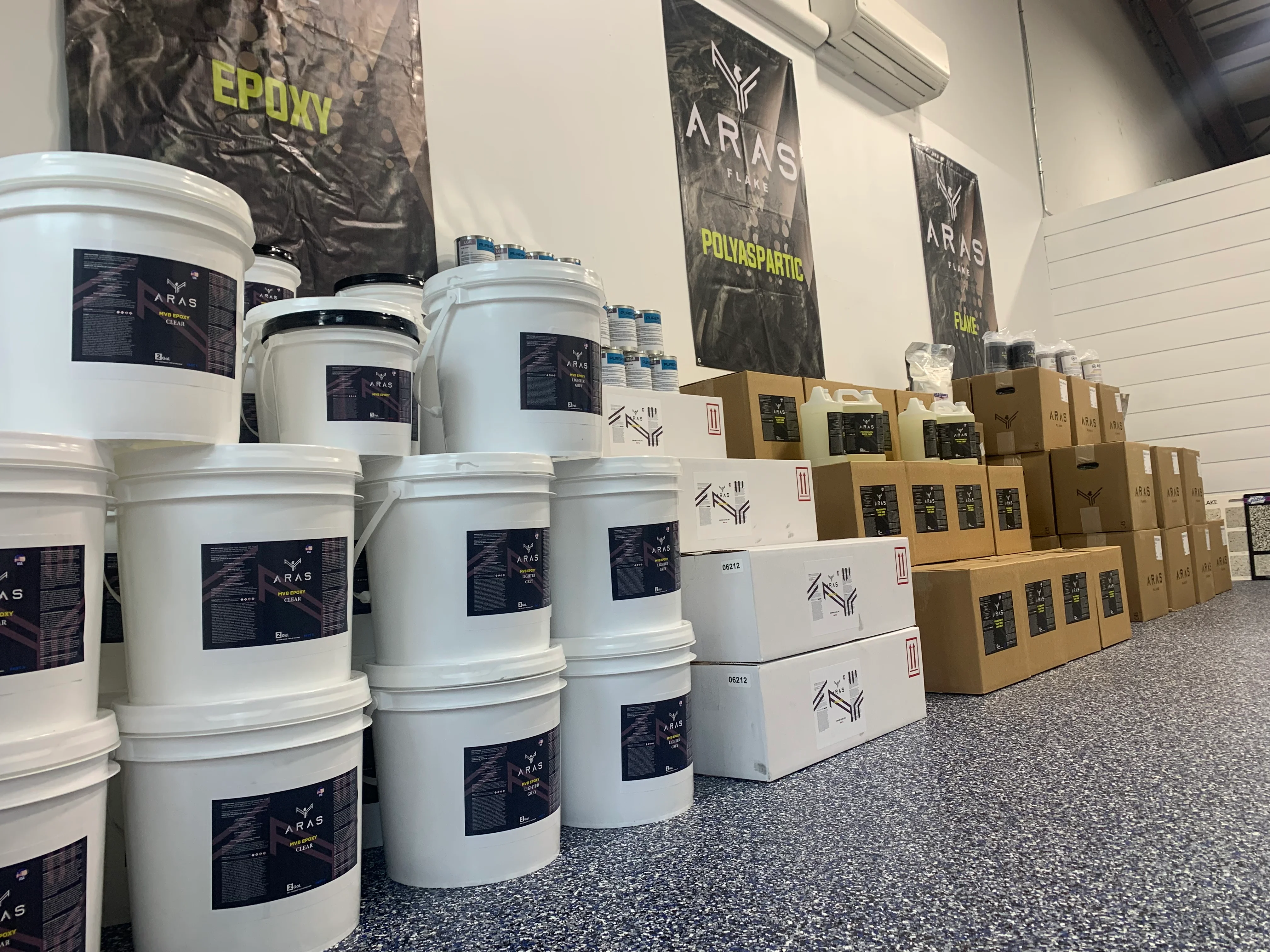 White buckets and cardboard boxes of epoxy and polyaspartic coatings in warehouse storage